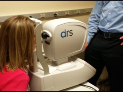 Female patient sits with her face resting on an eye screening camera.  