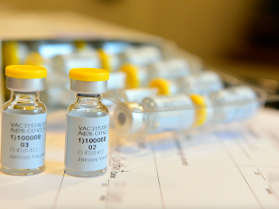 Vials of Janssen/Johnson & Johnson COVID-19 Vaccine Candidate sit on a desk. They are small clear vials with yellow lids and black and white labels.  