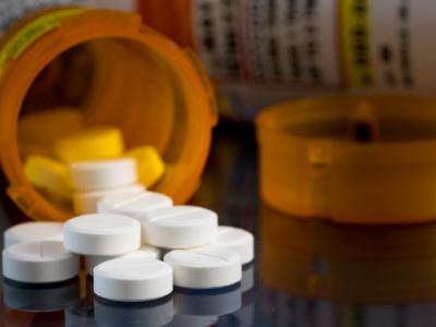 close-up of two orange prescription bottles lying on their side on a table, with white circular tablets spilling out of one of them. 