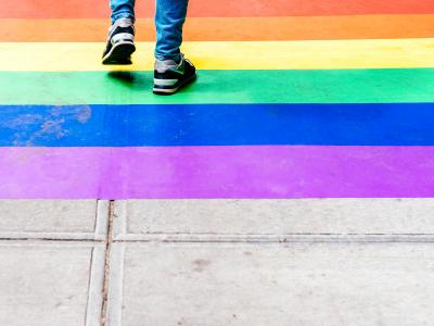 Shins and feet of a teen are shown walking over rainbow pavement. 