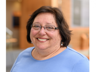 Headshot of Linda Dwoskin, PhD. She's a white middle-aged woman with chin-length dark brown hair, thin-framed rectangular glasses, and pearl earrings. She's wearing a periwinkle shirt and smiling. 