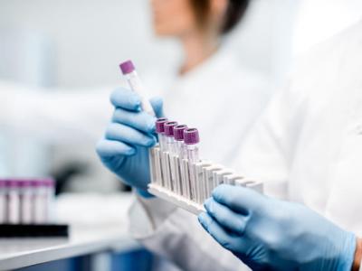 Close-up shot of hands in blue gloves handling a rack of test tubes in a lab. 