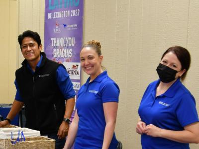 Three CCTS team members--Richard Sanchez, Ashley Hall, and Katie Schill, stand behind a long table wearing blue polo shirts and smiling. 