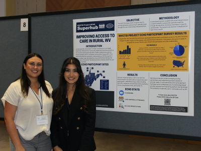 Two female college students stand in front of a research poster about improving access to healthcare in rural West Virginia. 