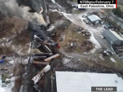 Screenshot from CNN's coverage of the train derailment and toxic spill/burn in East Palestine Ohio. The bleak image is an areal view of the burned-out train derailment with smoke still rising from the jumbled train cars. 