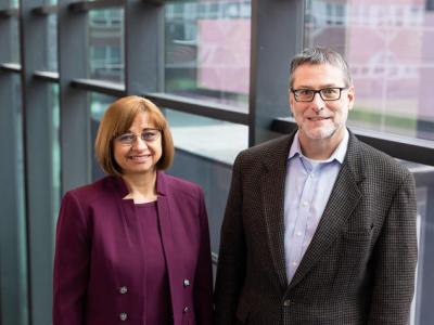 Svetla Slavova and Jeff Talbert stand side by side in front of a wall that's floor-to-ceiling windows. She is on the left, wearing a dark purple suit; her hair is a chin-length bob, she's wearing glasses and smiling. Talbert is on the right, wearing a gray blazer with a blight blue shirt beneath. He has short gray hair and dark-rimmed rectangular glasses. 