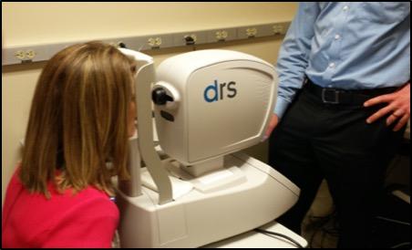 Female patient sits with her face resting on an eye screening camera.