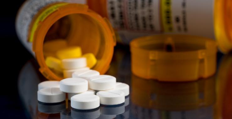 close-up of two orange prescription bottles lying on their side on a table, with white circular tablets spilling out of one of them. 