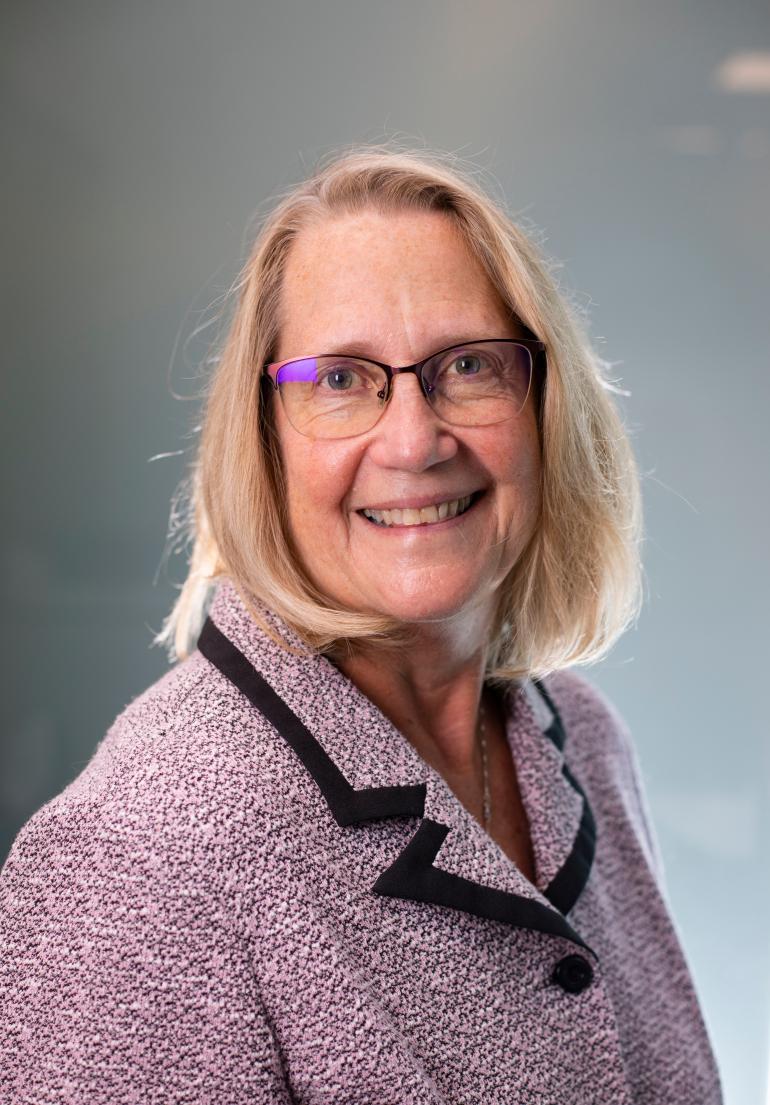 Photo of Linda Rice from the chest up. She has shoulder-length, straight blond hair and is wearing glasses and a mauve tweed blazer.