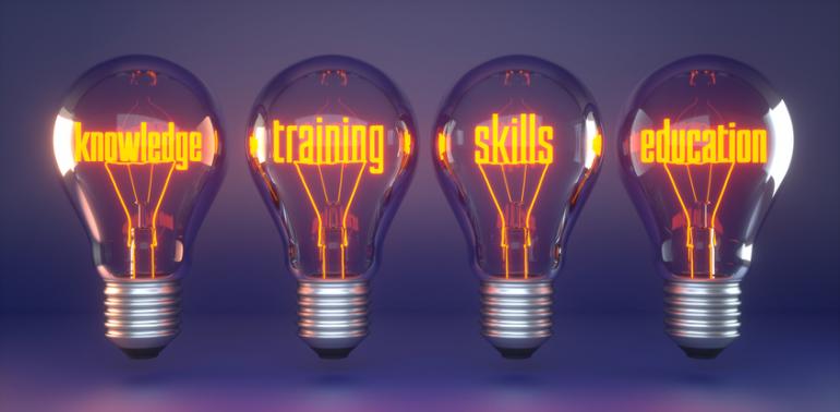 Four translucent lightbulbs float against a dark purple background. Inside each bulb the illuminated tungsten is shaped into a word: knowledge, training, skills, and education. 
