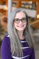 Photo of Dr. Amy Meadows, a white woman with long, straight gray hair and brown glasses. She's wearing a long sleeve dark purple shirt and smiling at the camera. 