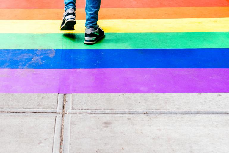 Shins and feet of a teen are shown walking over rainbow pavement. 