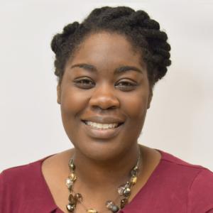 Headshot of Dr. Brittany Smalls, a Black woman in her 30s. She's smiling at the camera and wearing a dark pink shirt, with her hair twisted back on their side. 