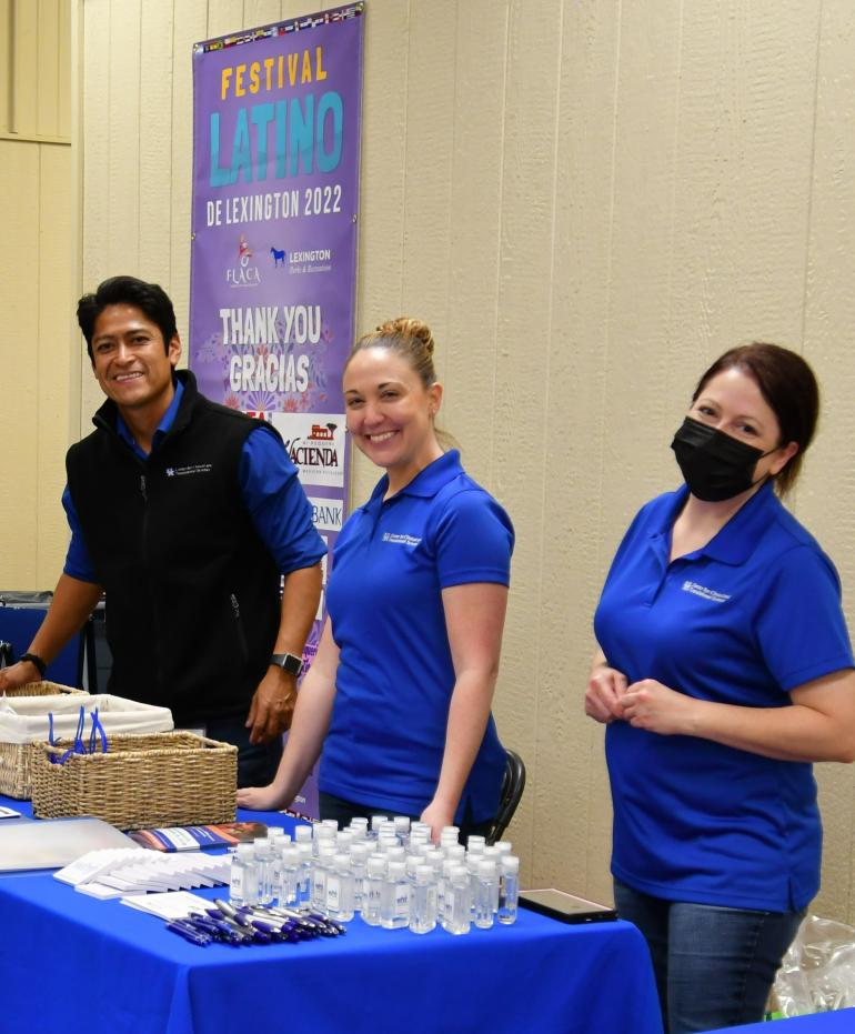 Three CCTS team members--Richard Sanchez, Ashley Hall, and Katie Schill, stand behind a long table wearing blue polo shirts and smiling. 