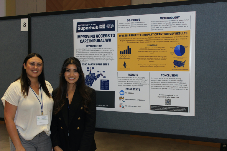Two female college students stand in front of a research poster about improving access to healthcare in rural West Virginia.