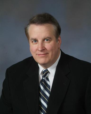 Faculty photo of Dr. Gerald Supinski, a white man in his 50s or 60s with kind eyes, wearing a black suit, white collared shirt, and gray striped tie. 
