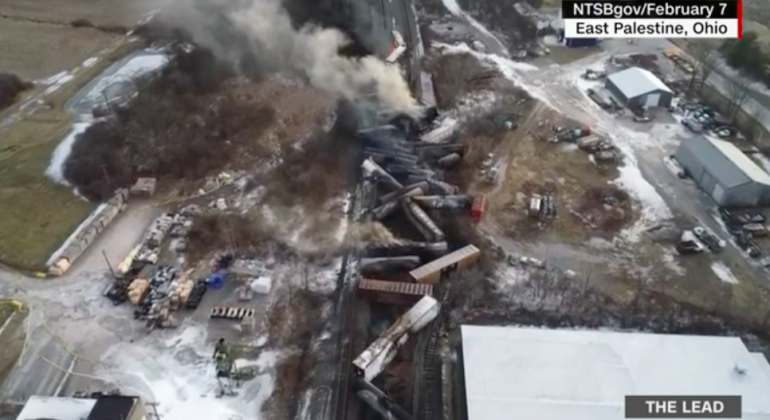 Screenshot from CNN's coverage of the train derailment and toxic spill/burn in East Palestine Ohio. The bleak image is an areal view of the burned-out train derailment with smoke still rising from the jumbled train cars. 