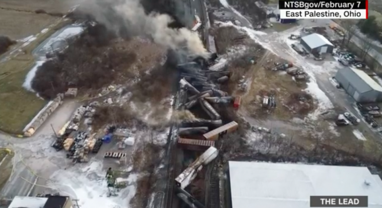 Screenshot from CNN's coverage of the train derailment and toxic spill/burn in East Palestine Ohio. The bleak image is an areal view of the burned-out train derailment with smoke still rising from the jumbled train cars.