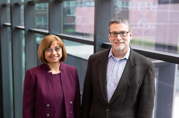 Svetla Slavova and Jeff Talbert stand side by side in front of a wall that's floor-to-ceiling windows. She is on the left, wearing a dark purple suit; her hair is a chin-length bob, she's wearing glasses and smiling. Talbert is on the right, wearing a gray blazer with a blight blue shirt beneath. He has short gray hair and dark-rimmed rectangular glasses. 