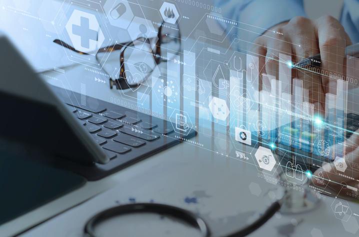 Stock image showing hands working at a laptop, and a stethoscope is on the desk. The image is overlaid with digital imagery of bar graphs and iconography.