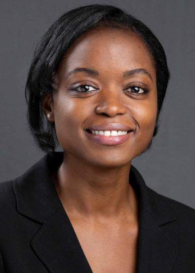 A headshot of Mautin Barry-Hundeyin, MD, PhD, a young Black woman with straight, chin-length hair. She's wearing a black suit jacket and smiling at the camera. There's a medium-gray backdrop. 