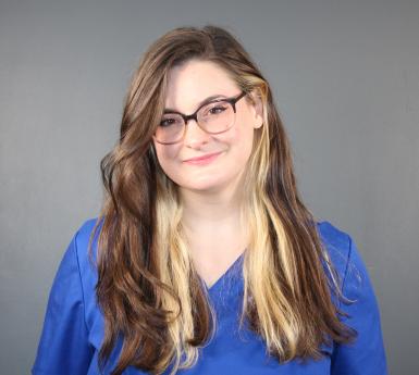 Photo of Regan Buckler, a young white woman with long two-toned brown and blonde hair. She's smiling at the camera, wearing glasses and a blue shirt. 