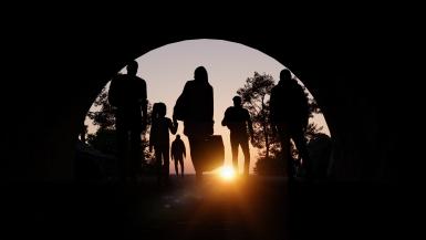 A group of people are walking out towards the sunset carrying backs. 