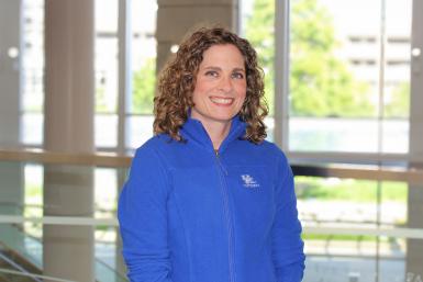 Dr. Krstyle Kuhs, a woman with shoulder-length curly brown hair, smiles at the camera. She's wearing a royal blue zip-up fleece.