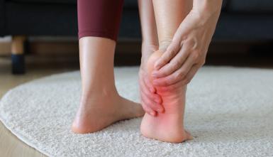 Woman massaging her painful foot and toes with red highlight on sole. Foot pain, plantar fasciitis, muscle strain and peripheral neuropathy concept for health care, physical therapy and wellness.