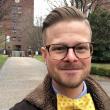 Headshot selfie of Aaron J. Kruse-Diehr, PhD, a white man with light brown, combed back hair, tortoise shell glasses, a brown coat, and a yellow bow tie. 