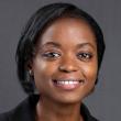 A headshot of Mautin Barry-Hundeyin, MD, PhD, a young Black woman with straight, chin-length hair. She's wearing a black suit jacket and smiling at the camera. There's a medium-gray backdrop. 