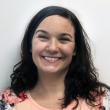 Headshot of Amanda Trout, PhD. She's a white woman in her 30s with wavy, almost black hair just past her shoulders. She's smiling at the camera and wearing a peach-colored shirt with red flowers. 