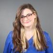 Photo of Regan Buckler, a young white woman with long two-toned brown and blonde hair. She's smiling at the camera, wearing glasses and a blue shirt. 