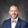 Professional headshot of Matthew Bush, a smiling, middle-aged white man with buzzed, dark hair and a closely-trimmed beard, wearing a dark blue suit jacket, white shirt, bow tie, and pocket square. 