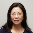 Headshot of an Asian woman with dark, straight hair falling just past her shoulders. She's wearing a navy shirt and rimless, rectangular glasses. 