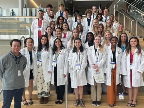 33 students from Frederick Douglass High School, all wearing white lab coats, and two of their teachers stand on the steps in Central Bank Center.