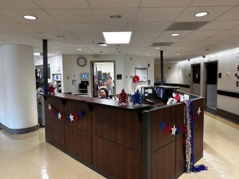 Lobby of the Clinical Research Unit. A clerk sits behind a wooden reception counter. Exam rooms are in the background. 