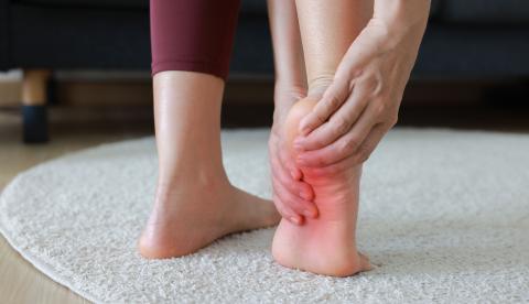 Woman massaging her painful foot and toes with red highlight on sole. 