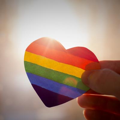 A heart in rainbow colors being held up to the sunlight.