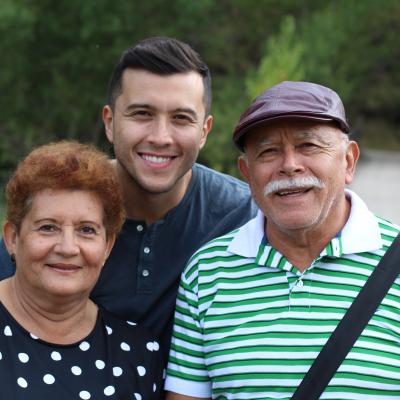 A young man stands in between his parents on a nature path with a footbridge in the background.