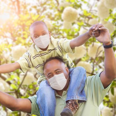 Black father with young son on his shoulder, both wearing masks. COVID