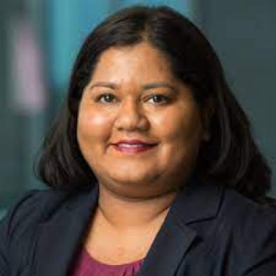 Headshot of Dr. Prajakta Adsul. She's has straight dark hair past he shoulders and is wearing a navy suit jacket with a dark red round-neck shirt beneath. She's smiling at the camera.